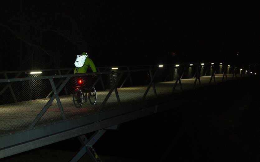 Fahrradfahrer auf spärlich beleuchteter Brücke, Rucksack reflektiert.