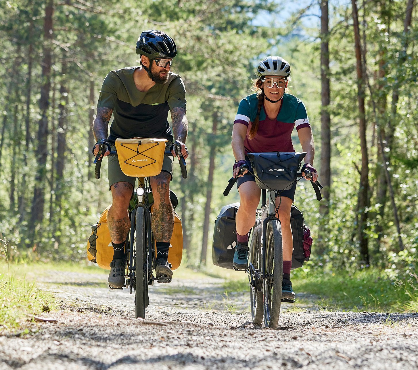 Zwei Radreisende auf Schotterweg im Wald mit kompletter Vaude-Taschenausrüstung – Naturgenuss und Outdoor-Feeling pur