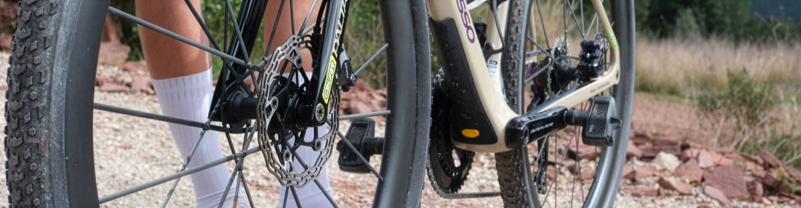 Close-up of a beige Basso Palta gravel bike with front wheel and disc brake on a gravel road.