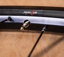 Detail photo: A thin road bike valve inserted into the large hole of a rim designed for Schrader valves.
