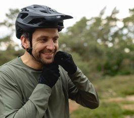 Portraitfoto: Ein ca 40 Jahre alter Mann mit dunklen Haaren und Bike-Handschuhen stellt den Kinnriemen seines schwarzen MTB Helms ein.