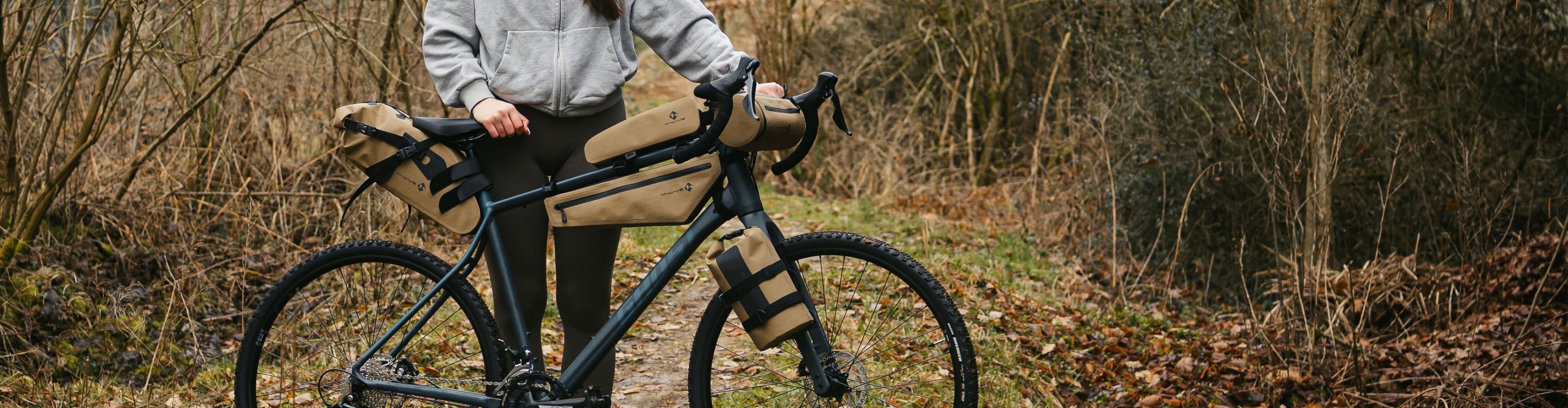 Person mit einem Gravelbike und beigen M-Wave Bikepacking-Taschen auf einem Waldweg