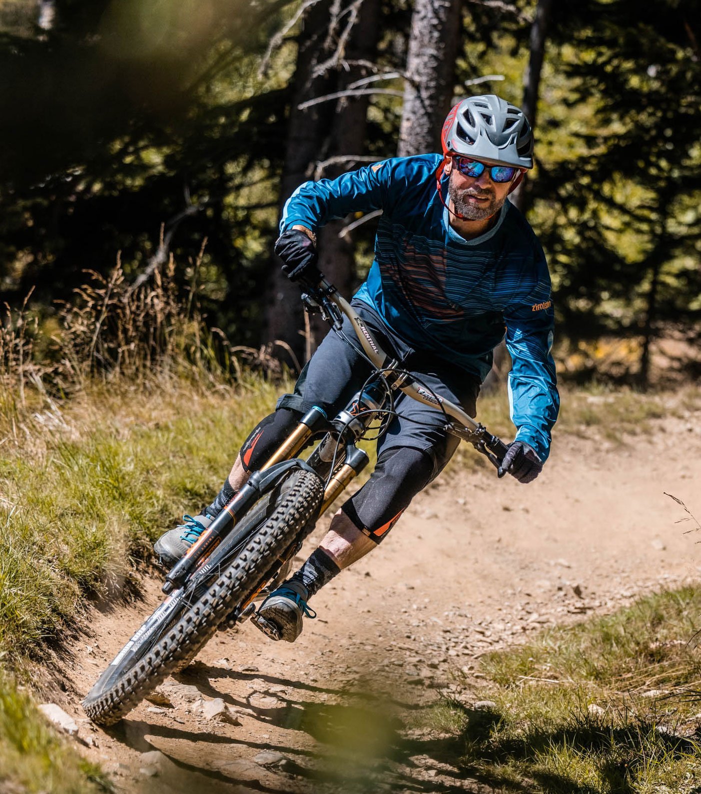 Mountainbiker in blauer Zimtstern MTB-Bekleidung fährt mit Helm und Brille eine staubige Kurve auf Waldtrail.