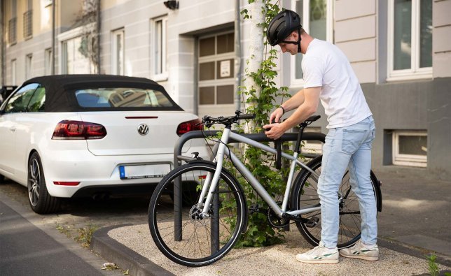 Hombre con casco asegurando su bicicleta con un candado de cadena a un soporte en la calle.