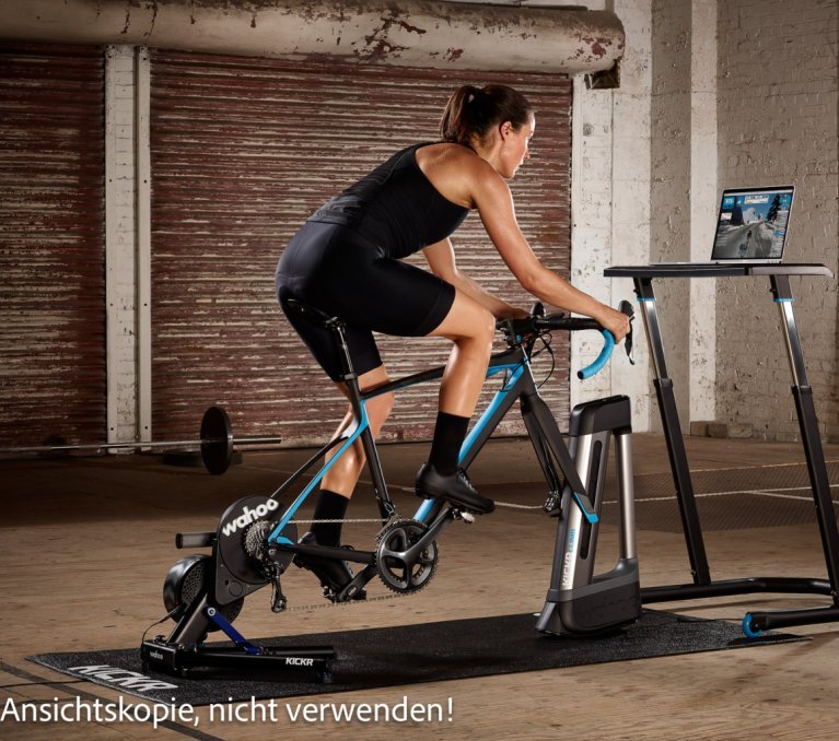 Persona pedaleando en un rodillo inteligente de interior mientras mira un portátil con software de entrenamiento.