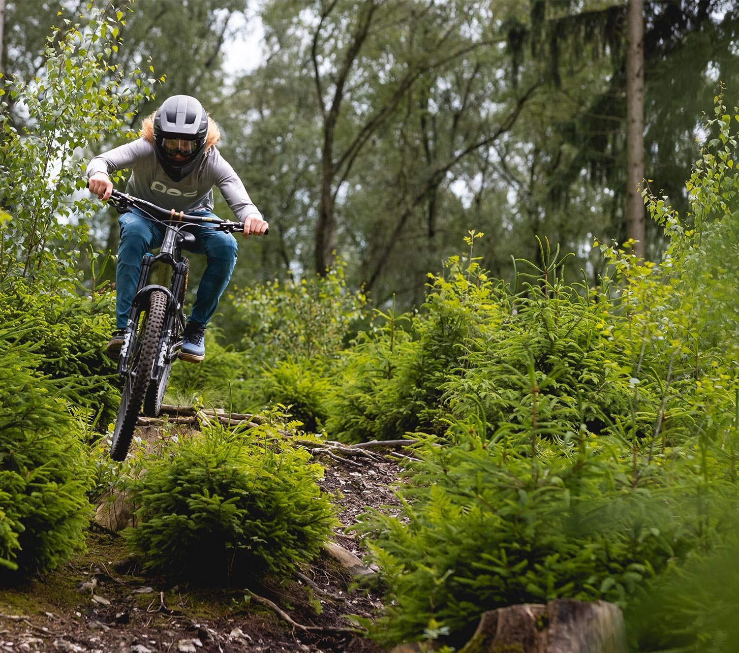 Vététiste roulant sur un sentier forestier avec racines et petites marches – scène illustrant des vêtements VTT respirants pour le printemps et l’été.