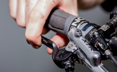 Gros plan d’une main actionnant le levier de frein d’un vélo pour vérifier le fonctionnement du frein récemment entretenu.