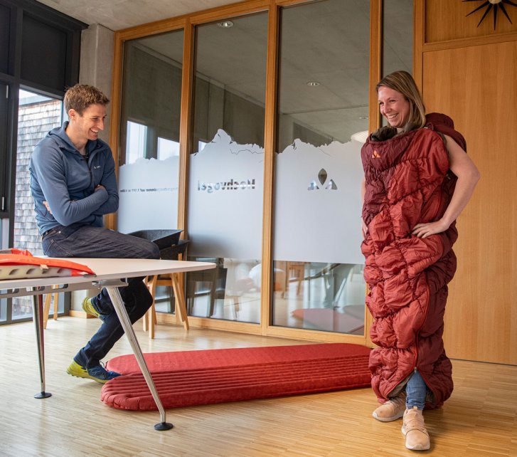 Svenja con el saco de dormir de la serie Meglis, puesto como chaqueta de cuerpo entero. Esto la divierte tanto a ella como a Markus de VAUDE.