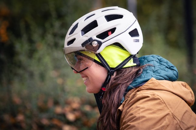 Side view of a young woman wearing a white bicycle helmet with a flip-up visor.