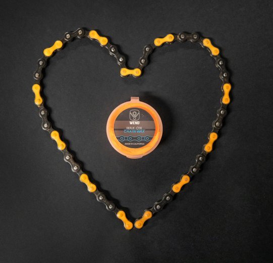 A chain is laid out in the shape of a heart. The chain is coloured orange with chain wax. 