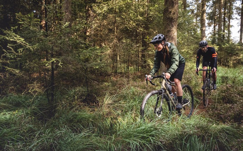 A man and a woman ride their gravel bikes along a forest path.