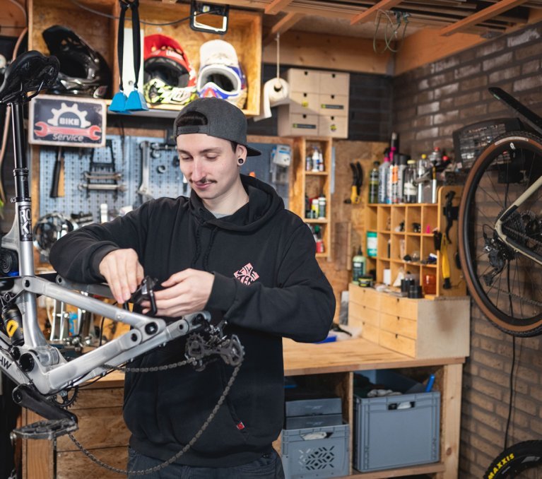 bc Mechaniker Pascal prüft die Hinterradbremse eines RAAW Mountainbikes in einer Hobby-Werkstatt.