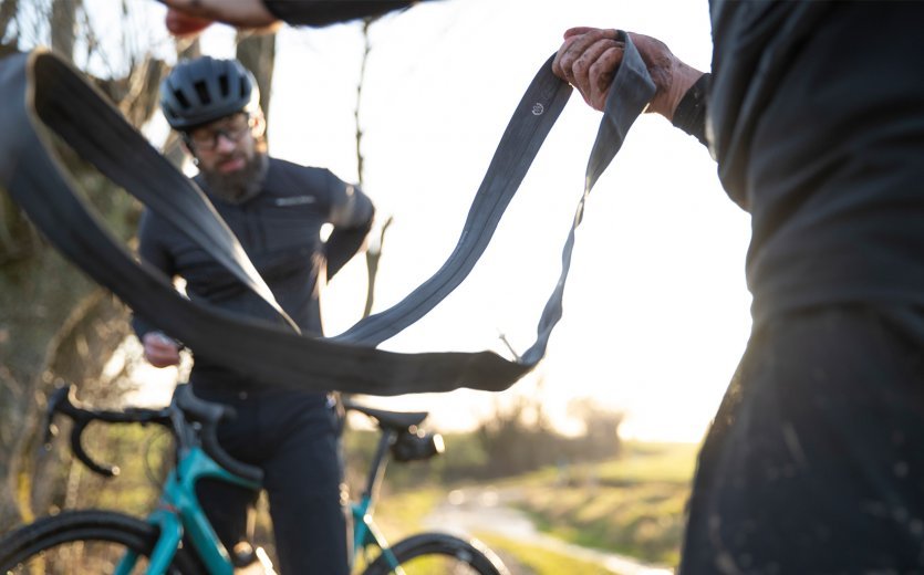 Deux cyclistes ont une crevaison pendant une sortie. Pendant que l'un sort une chambre à air, l'autre cherche une cartouche de CO2 dans sa poche arrière.