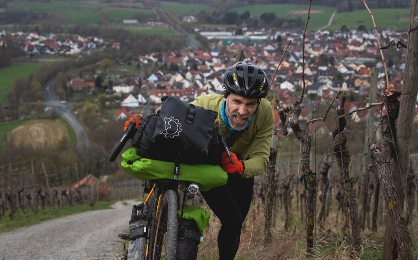 Ein Teilnehmer schiebt mit schmerzverzerrtem Gesicht sein Bike den Weinberg hoch. Man sieht im Hintergrund, wie unfassbar steil die Passage ist. 