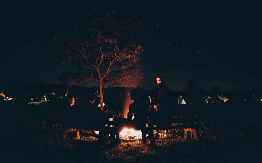 Four gravel bikers sit relaxed around a campfire at night.