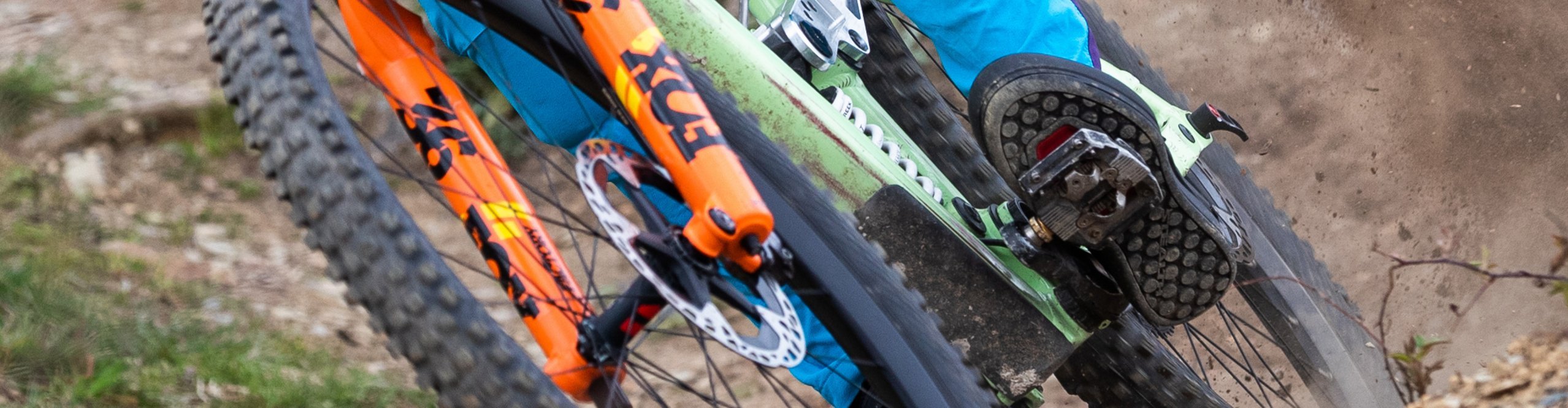 Mountainbiker steht auf Trail fest im Pedal, Schotter staubt auf