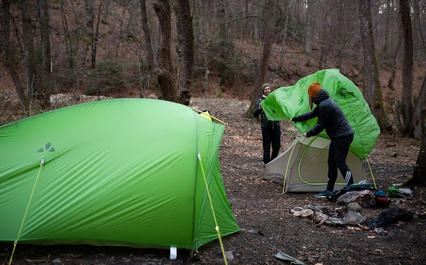 Rainer und Svenja von bc bauen ein Zelt auf. Im Vordergrund steht ein bereits aufgerichtetes Zelt von VAUDE. 
