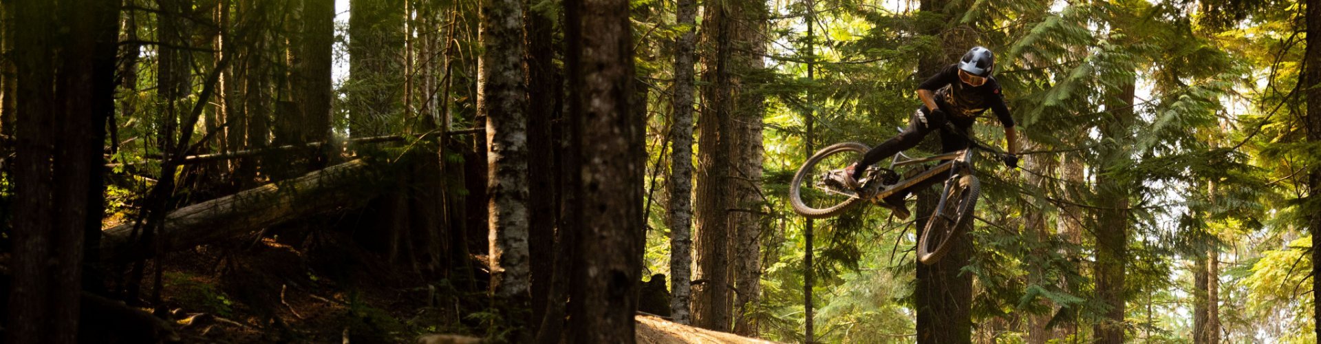 Christoph from the bc Team whips his bike during a jump with his MTB. He’s riding in the forest.