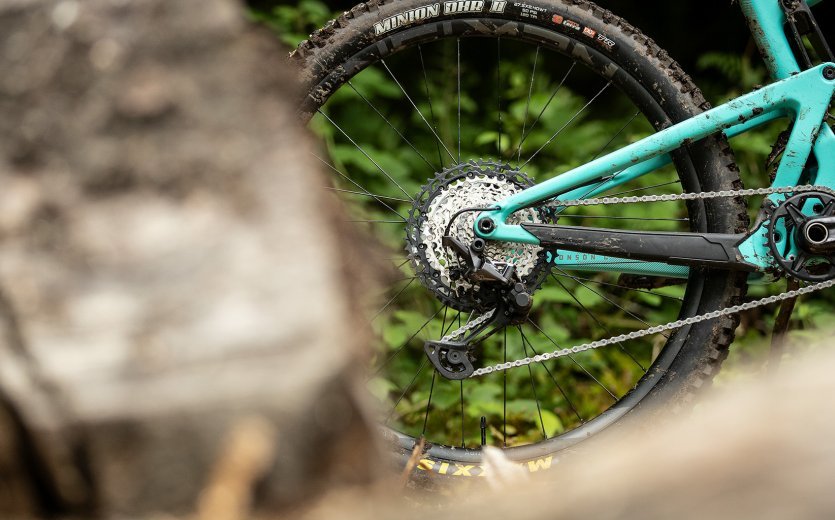The drive side of a turquoise mountain bike can be seen behind a blurred stone.