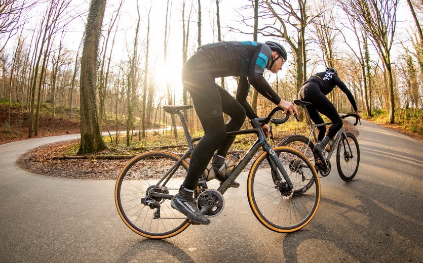 Two road cyclists, riding Scott and Factor bikes, ride uphill in autumn weather.
