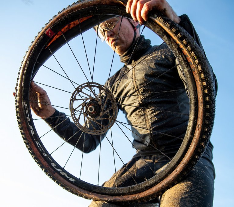 Ein Biker montiert nach einer Panne einen neuen Schlauch zwischen Felge und Reifen seines Gravelbikes.