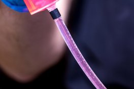 A syringe hose with clear fluid shows air bubbles rising upward.