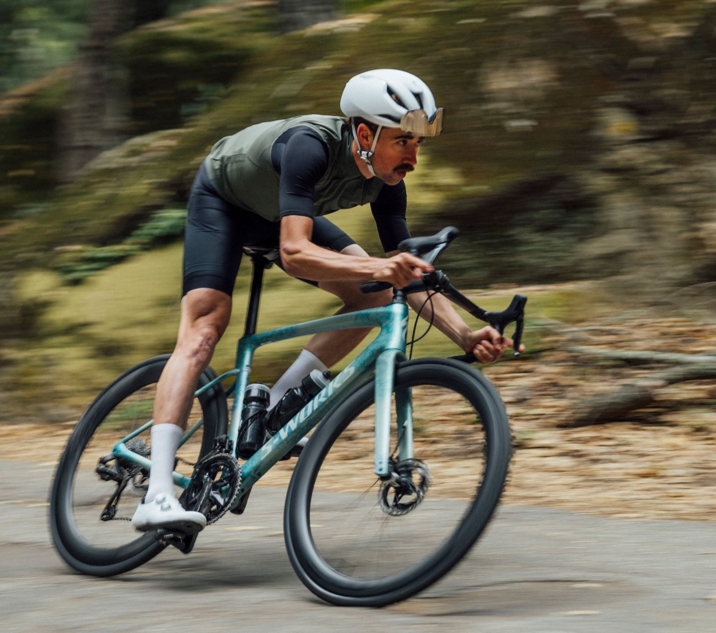 Sportlicher Rennradfahrer in aerodynamischer Position fährt ein Specialized Rennrad auf kurviger Straße im Wald – Performance-Roadbike für ambitioniertes Training und schnelles Straßenfahren.
