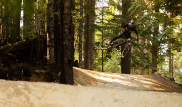 Christoph aus dem bc Team stellt während eines Sprungs mit seinem MTB das Rad quer. Er befindet sich im Wald.