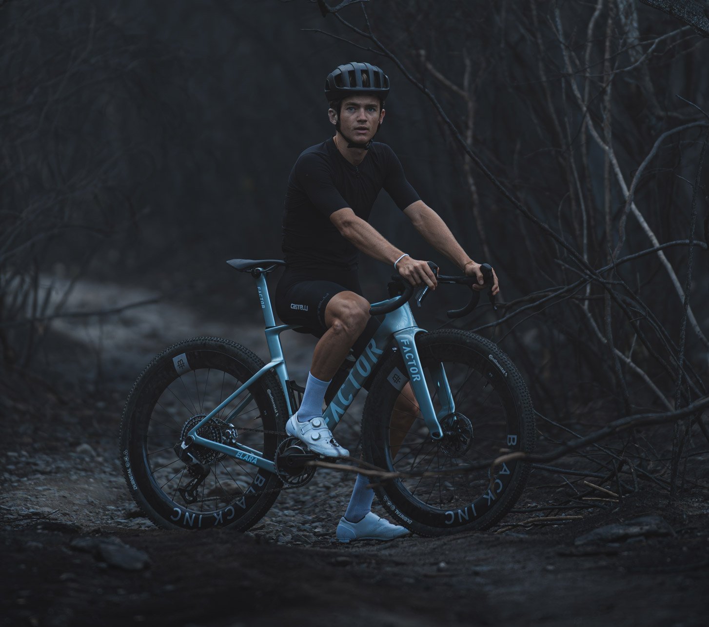 Ciclista de gravel sobre una Factor Elara azul en un camino pedregoso de un bosque oscuro.