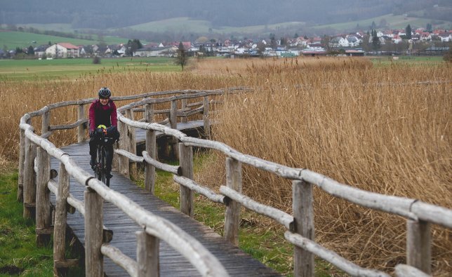 Linda fährt über einen Steg, der durch eine Moorlandschaft führt. 