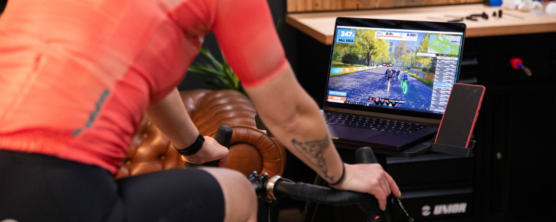 Gros plan sur une jeune femme qui pédale sur un vélo d'appartement dans son salon, tout en suivant son entraînement Zwift sur son ordinateur portable et en se concentrant sur le parcours virtuel.