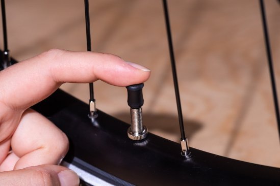 A finger presses a black cap onto a Schwalbe Clik Valve.