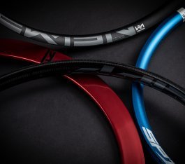 Vier Fahrrad-Felgen in Schwarz, Rot und Blau liegen auf einer dunklen Fläche