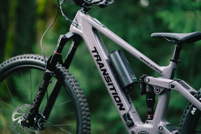 Close-up of a grey Transition Regulator SX E-MTB in the forest: focus on the Bosch range extender mounted on the bottle cage in the frame triangle