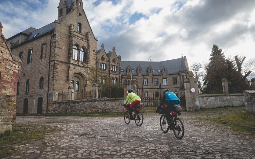 2 Teilnehmer fahren an einem alten Schloss vorbei über Kopfsteinpflaster.