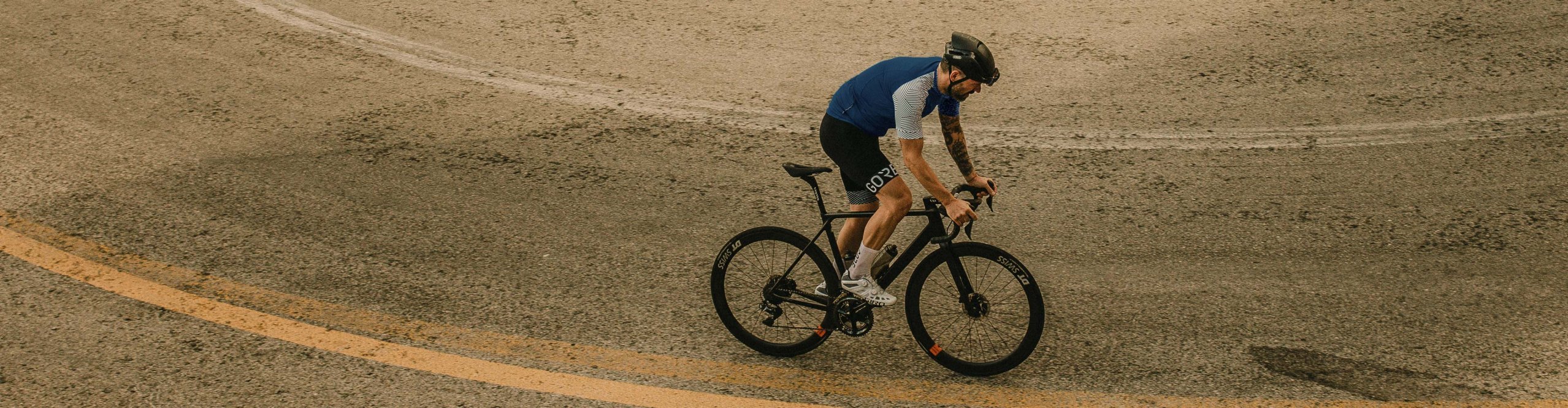 Cycliste sur route portant des vêtements Gore Wear roulant sur une route asphaltée sinueuse vue de dessus