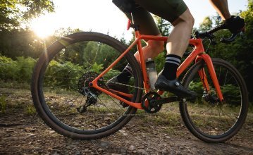 Björn from the bc Team rides an OPEN gravel bike over a dirt road. The bike is the focus of the picture.