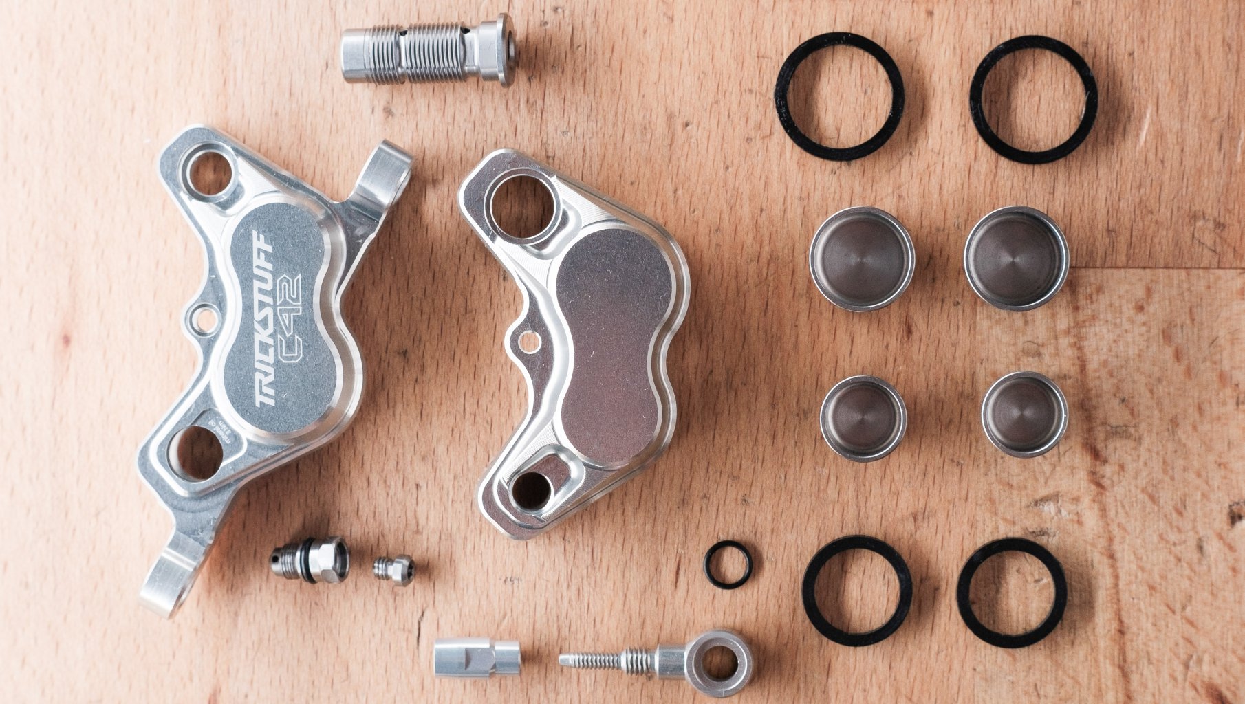 Las piezas de una pinza de freno Trickstuff C42 están distribuidas sobre una superficie de madera de haya.