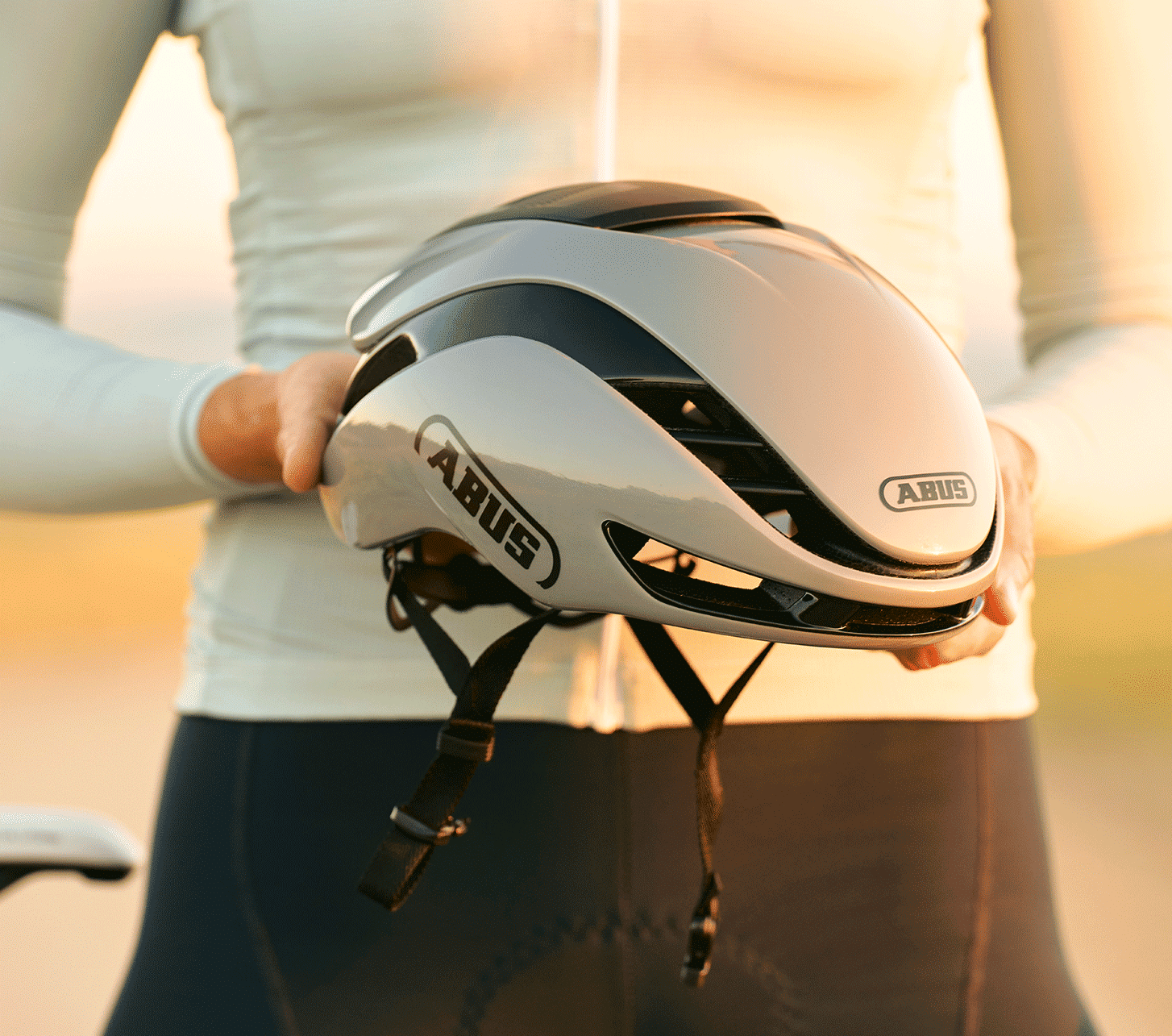 Cycliste sur route tenant un casque de vélo aérodynamique ABUS argenté dans ses mains.