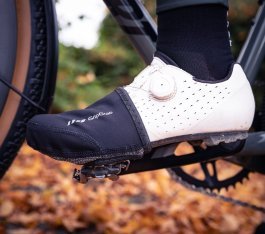 Pie izquierdo con zapatilla gravel blanca y una toe cap negra encima delantera.