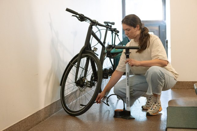 A young woman crouches in a hallway next to a bicycle and a white SKS floor pump.