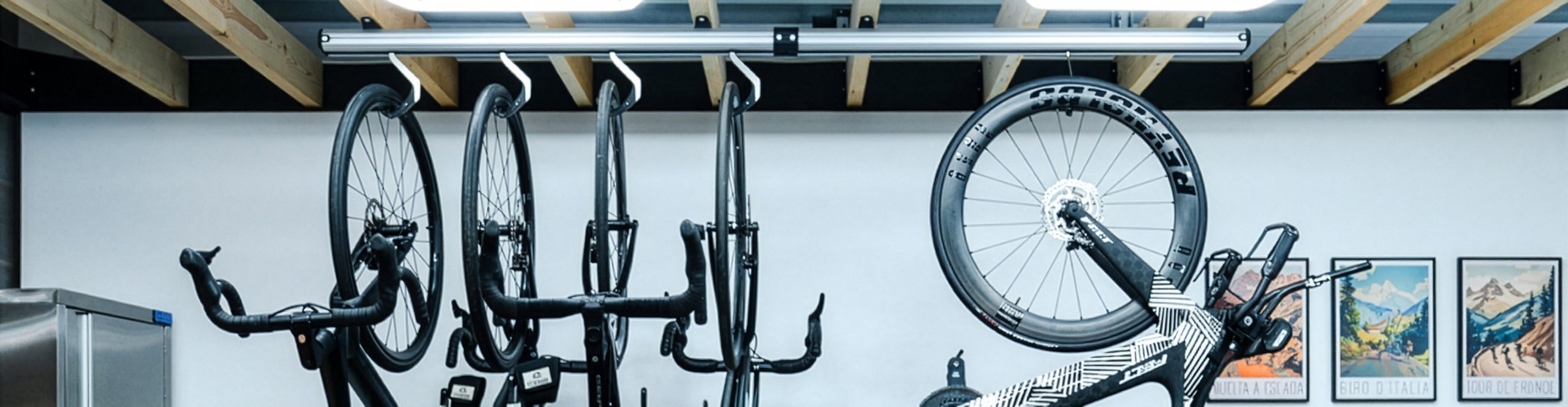 Multiple road bikes and a triathlon bike hang space-saving on a wall-mounted bike storage rack in a modern workshop.