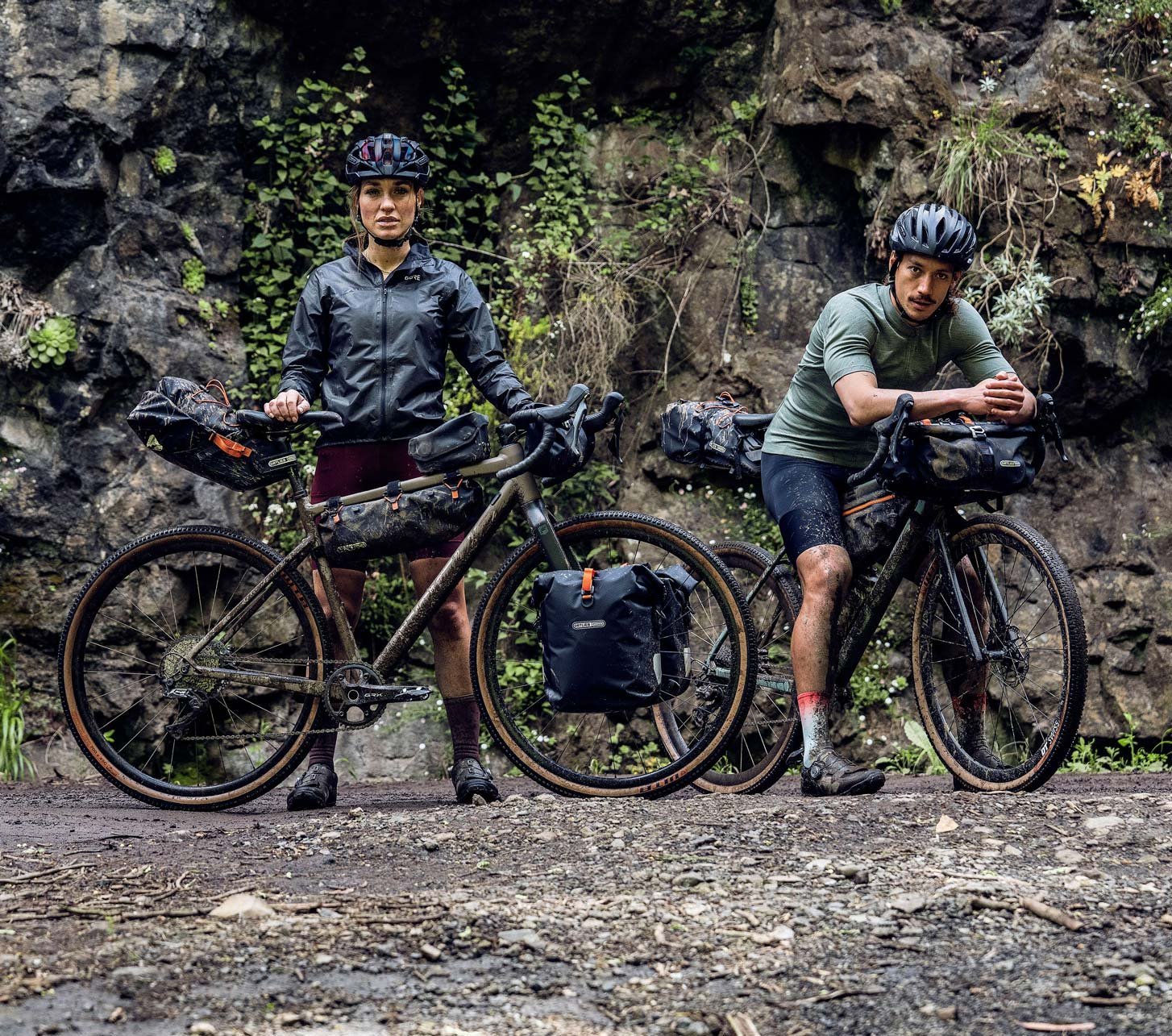 Two bikepackers with gravel bikes and ORTLIEB bikepacking bags on a gravel trail in front of a rocky cliff