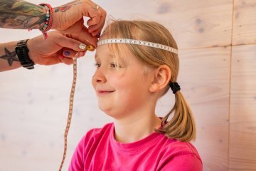 Child having head circumference measured with a tape to find the correct size for a kids bike helmet.