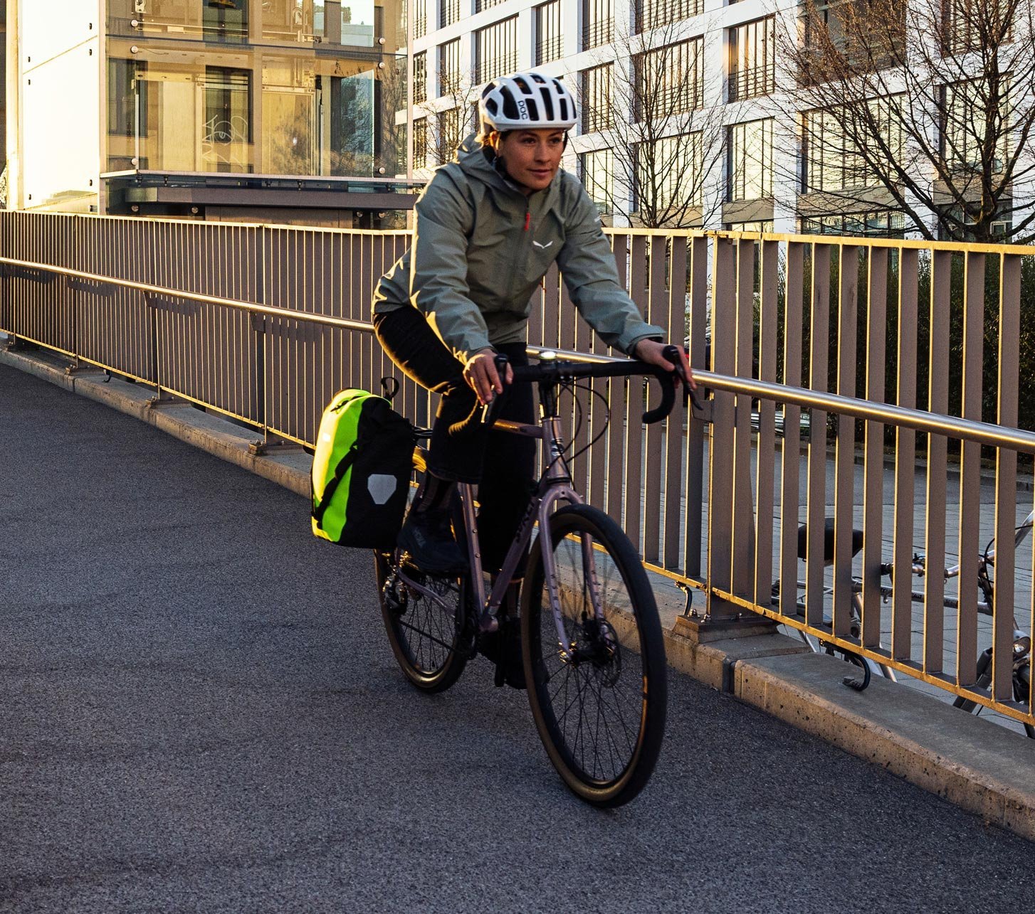 Radfahrerin mit wasserdichter ORTLIEB Fahrradtasche am Gepäckträger fährt über eine Brücke in der Stadt