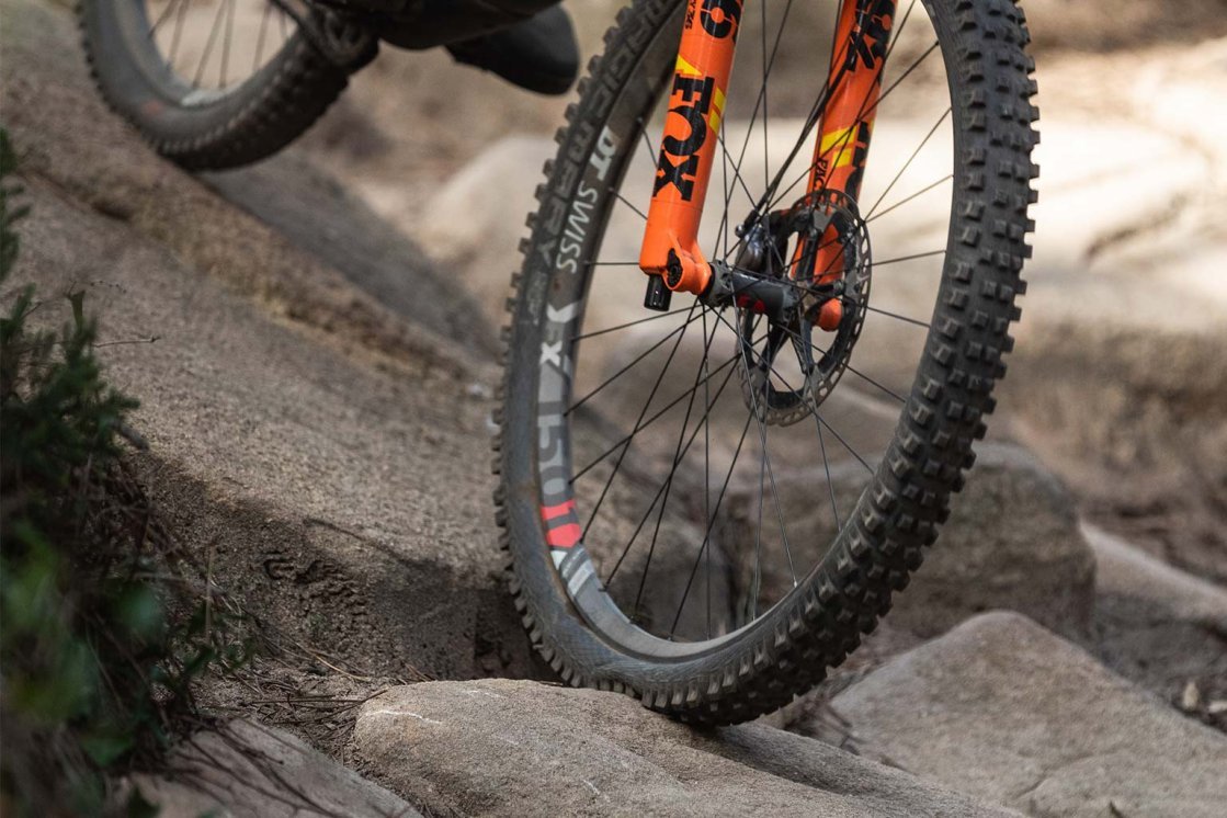 Rueda delantera de una bicicleta de montaña rodando sobre piedras en un sendero.