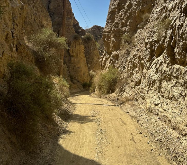Ein staubig-sandiger Canyon. Eine Telegrafenleitung säumt die enge Schotterstraße, ein kleiner Fleck blauen Himmels ziert den oberen Bildrand.