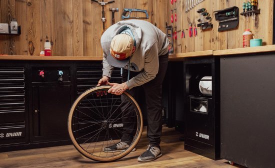 Personne montant un pneu gravel à la main sur une jante de vélo dans un atelier.