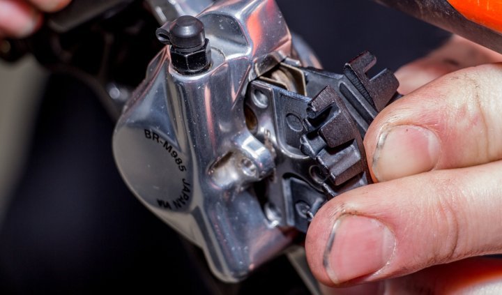 Nahaufnahme einer Hand, die neue Shimano-Bremsbeläge in einen BR-M985-Bremssattel einschiebt.