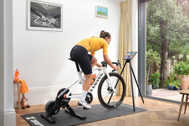 A woman trains on a Wahoo Kickr Core smart trainer with a white Canyon road bike in a bright room with wooden floors.